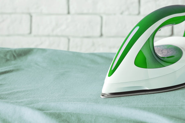 特写的热熨斗使熨烫板上起皱的绿色衣服光滑图片下载