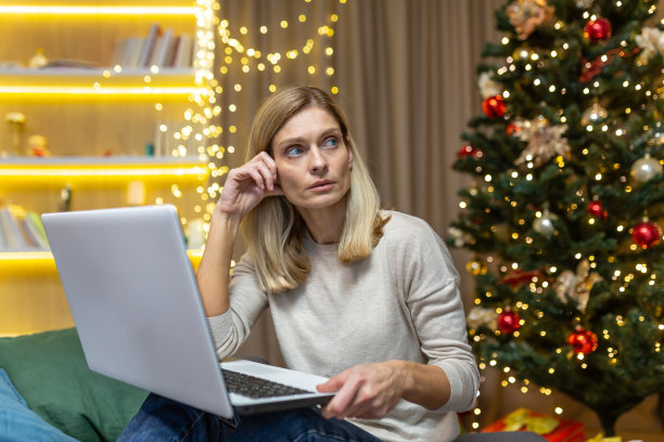 悲伤的女人坐在家里的沙发上，坐在笔记本电脑旁为圣诞节庆祝新年，沮丧的家庭主妇在圣诞树旁图片下载