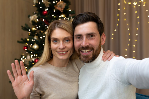 已婚夫妇，通过在线视频电话祝贺新年快乐，远程坐在家里的沙发上看着智能手机摄像头。直播的问候。手机凸轮视图图片下载