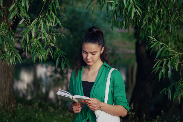 女学生在城市公园的柳树下看书。图片下载