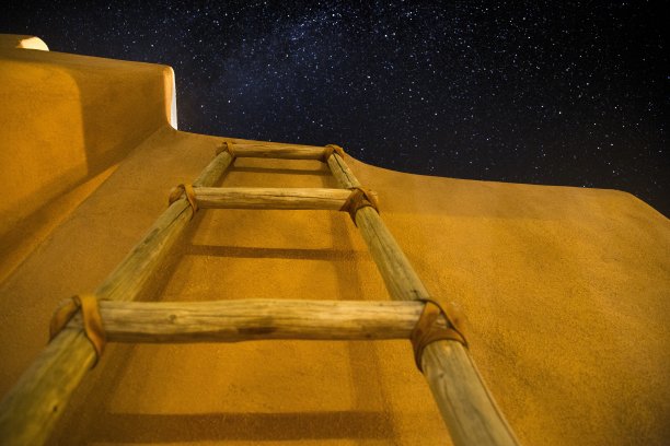 在满是星星的黑暗天空下，低角度拍摄建筑附近的木梯子图片下载