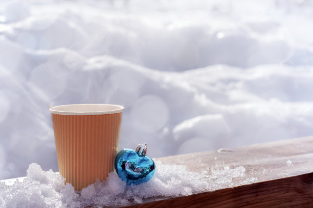 咖啡或茶和心形圣诞玩具放在咖啡馆的木制户外桌子上，背景是雪堆和复制空间。圣诞节假期，冬天散步休息喝热饮图片下载