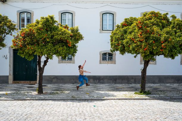 在老城法罗，一名亚洲妇女跳着去攀爬郁郁葱葱的橘子树图片下载