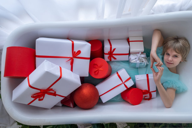 少女在装满礼品盒的浴缸里泡澡，圣诞节概念图片下载