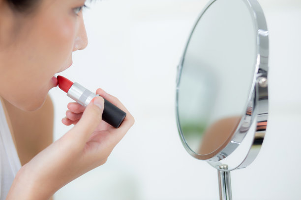 美丽的年轻亚洲女性涂口红红色的嘴，美丽的女孩看着镜子化妆化妆的嘴唇优雅，化妆的女性性感，护肤和健康的概念。图片下载