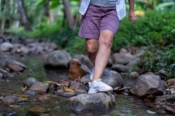 照片拍摄在背包徒步旅行者的脚和腿走路踩过岩石在水流图片下载