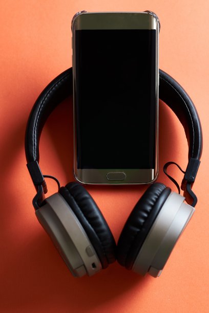 橙色表面上的无线耳机和手机特写镜头图片下载