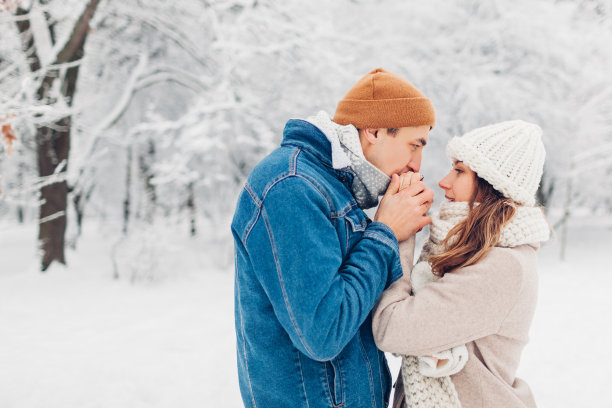 在大雪纷飞的冬日公园里，男人用呼吸温暖着女人的手。爱的情侣在户外散步图片下载