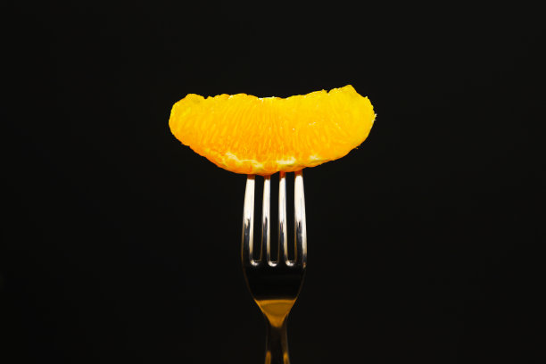 在黑暗的灯光下叉子上的一片橙子。特写镜头图片下载