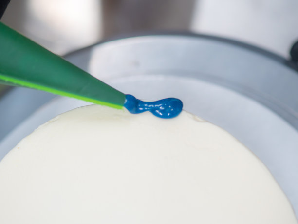 近手糕点厨师设计师顶部的霜白色蛋糕与蓝色滴填充袋图片下载