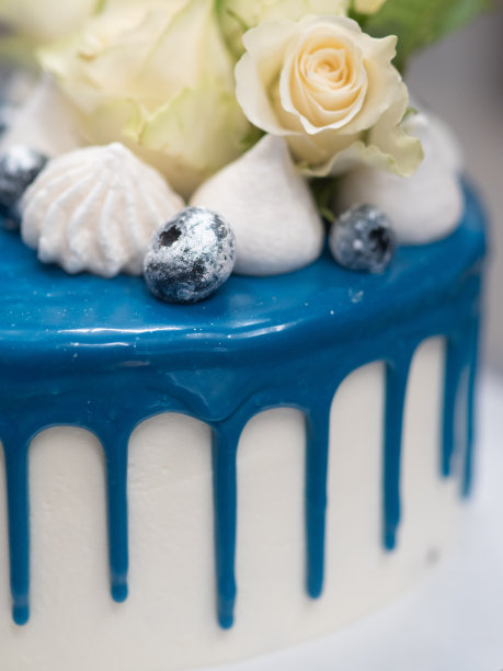 宏观厨师装饰顶部的蓝白色磨砂蛋糕与马卡龙蛋白和真正的花朵图片下载