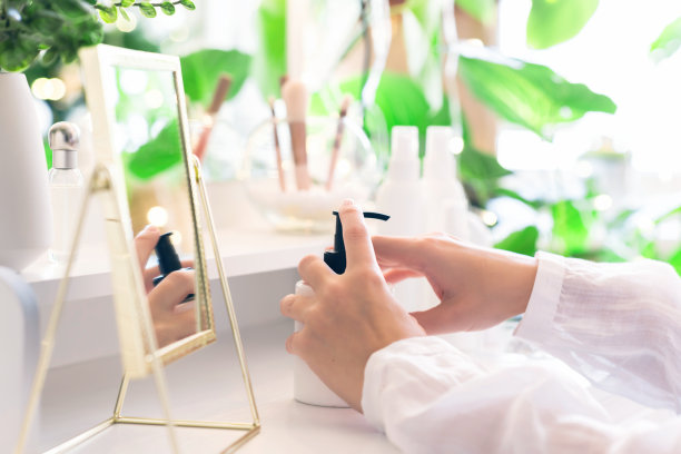 妇女在她的手上涂抹每日面霜坐在梳妆台附近，化妆配件和桌子镜子。图片下载