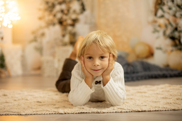 可爱的金发幼童学龄前男孩，阅读一本书和打开礼物在圣诞节在舒适的家图片下载