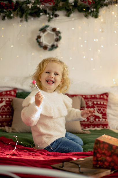 可爱的小卷毛女孩在冬天的圣诞毛衣，坐在舒适的房间，为圣诞节装饰图片下载