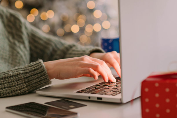 圣诞节网购，冬季打折促销，在家网购。女性的手放在笔记本电脑上，带有模糊的散景灯图片下载