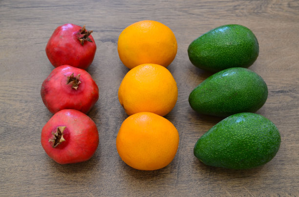 木桌上放着新鲜成熟的热带水果。石榴、橘子、鳄梨。红色,黄色,绿色。异域水果，纯素食品或饮食概念。图片下载