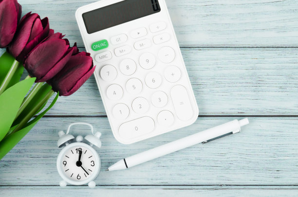 平铺，俯瞰办公木桌书桌。工作空间，闹钟，计算器，笔，红色郁金香花在蓝色的木制背景。图片下载