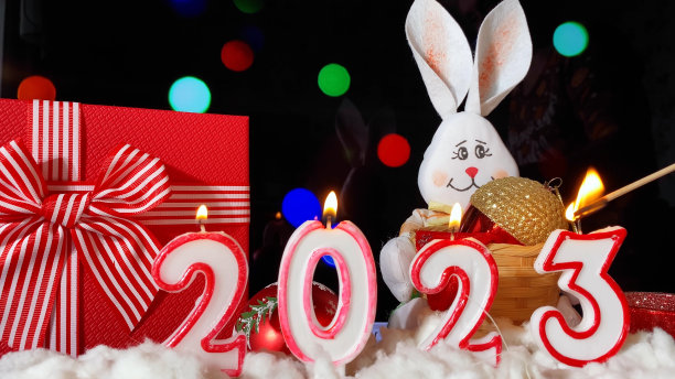 2023年新年快乐。蜡烛和白色的兔子在黑色的节日闪闪发光的背景制作的2023。图片下载