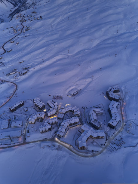 从鸟瞰图上可以看到，在日落时分，沿着蜿蜒曲折的道路，山村小屋被夜晚的路灯照亮。日落时有雪粉斜坡的滑雪场。乔治亚州的新古道里。图片下载