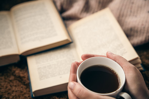 特写，女性手中的一杯茶在模糊的书籍背景上。图片下载