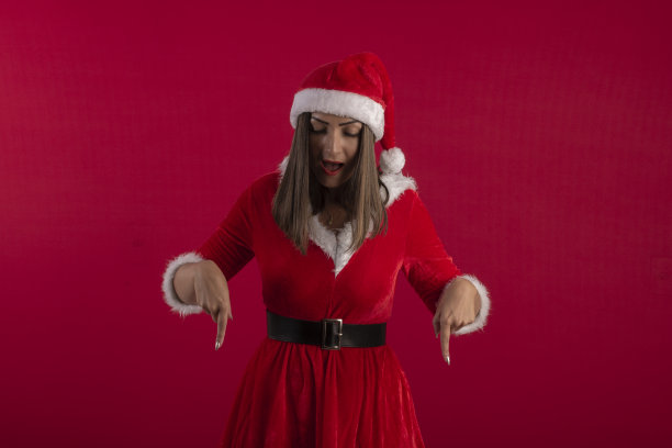 年轻女子在圣诞老人的服装和帽子，在工作室照片与蓝色背景和圣诞主题图片下载