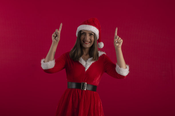 年轻女子在圣诞老人的服装和帽子，在工作室照片与蓝色背景和圣诞主题图片下载