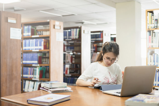 一名亚洲妇女在图书馆的桌子上用平板电脑和笔记本电脑搜索信息。图片下载