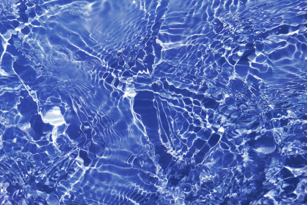离焦模糊透明蓝色清澈平静的水面纹理与飞溅和气泡。新潮抽象的自然背景。阳光下的水波与复制空间。蓝色水彩闪闪发光图片下载