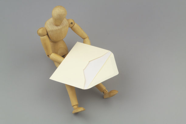 木制假人拿着黄色信封和灰色背景的信。图片下载