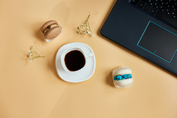 平铺，俯瞰办公桌办公桌，工作区与笔记本电脑，马卡龙与咖啡杯和鲜花，在橙色背景，从家里工作，遥远的工作。图片下载