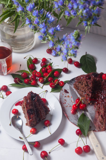 巧克力蛋糕配甜樱桃，一杯茶和一束白底蓝花。图片下载