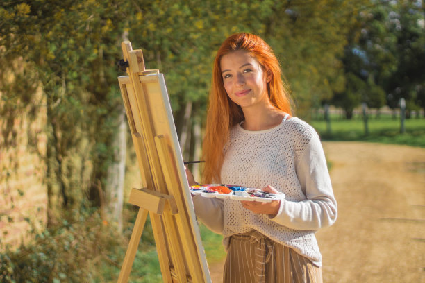 阳光下拍摄的一个红头发的女性绘画板与调色板在公园里图片下载