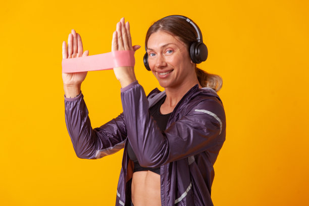 肖像一个微笑的运动妇女戴着耳机与健身带在一个黄色的背景。健康的生活方式。健美操与健身图片下载