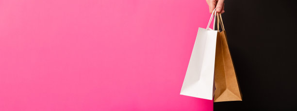 黑色星期五横幅。女性手拿两个粉色和黑色背景的购物袋。手里拿着白色和棕色的工艺空白纸袋。黑色星期五减价、打折、购物和生态概念。图片下载