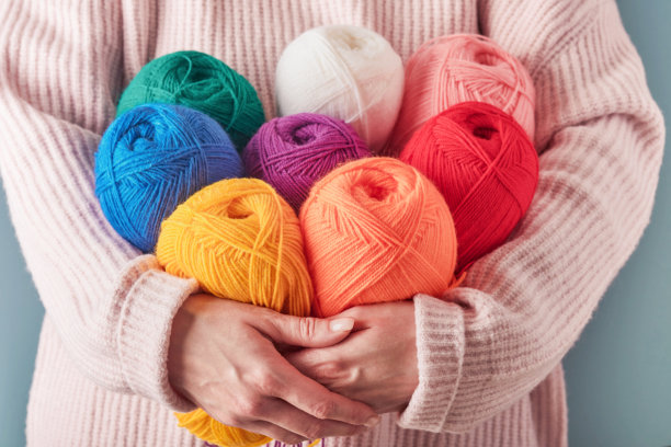 在蓝色的背景上，雌性抱着彩色或多色的毛线。许多彩色的线球特写。针线活或针织概念。图片下载