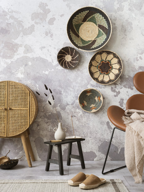 富有创意的民族风格客厅内饰，色彩鲜艳的篮子，藤条餐具柜，棕色扶手椅和优雅的个人配饰。灰色的混凝土墙。家居装饰。模板。图片下载