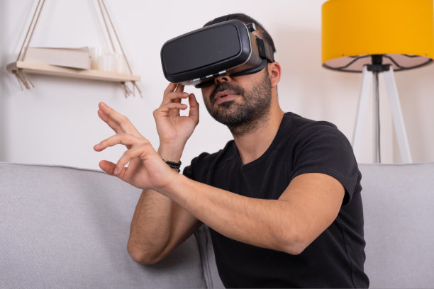 年轻人戴着VR眼镜头戴式耳机在家与虚拟现实互动，做手势。未来科技，教育电子游戏图片下载