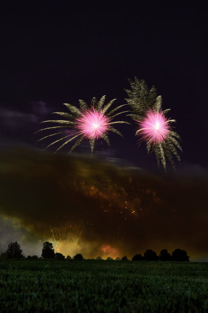 粉红色的星星和黄色的喷泉映衬着漆黑的夜空。绿色草地和林木线。非常适合西尔维斯特和新年。潮湿的空气中浓烟滚滚。德国,Ostfildern。图片下载