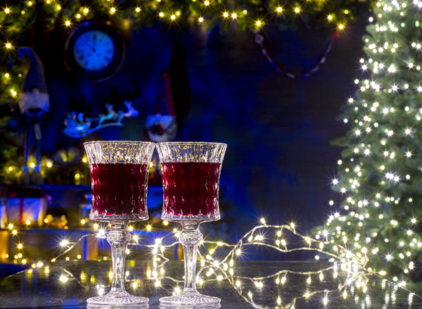 圣诞彩灯映衬下的一对红酒杯。图片下载