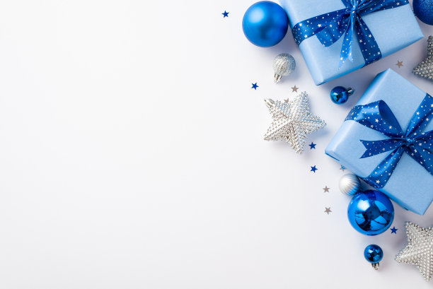 新年美学观念。顶视图照片蓝色白色银饰大礼物盒与丝带蝴蝶结闪闪发光的明星饰品和纸屑在孤立的白色背景与复制空间图片下载