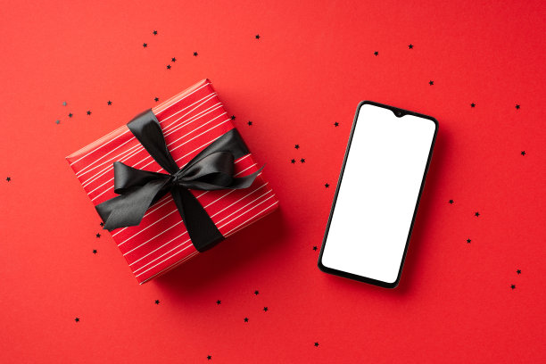 网络星期一的概念。俯视照片的智能手机红色礼盒丝带蝴蝶结和彩纸上孤立的红色背景与空白图片下载