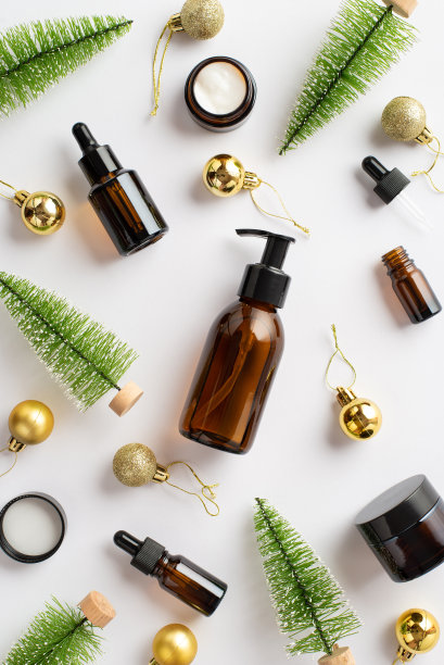 冬季护肤化妆品概念。顶视图垂直照片琥珀泵瓶奶油罐滴管瓶圣诞树玩具和金色的小玩意在孤立的白色背景图片下载