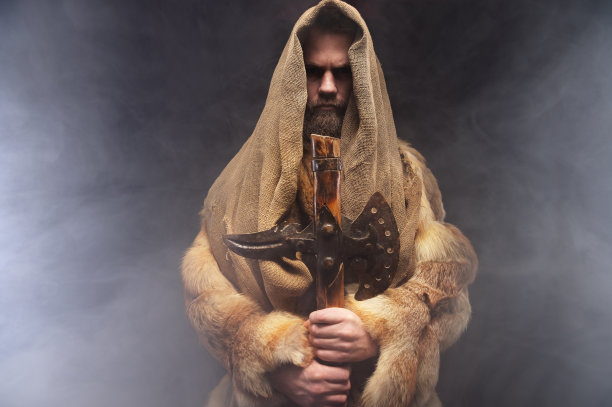 一个勇敢严肃的人的肖像，一个中世纪的战士或僧侣穿着长袍，手持斧头，在一个黑暗的背景上。时代、历史、文艺复兴风格的比较图片下载