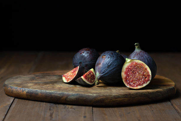 成熟的湿无花果放在木桌的砧板上。整的和切片的水果。黑色的背景图片下载