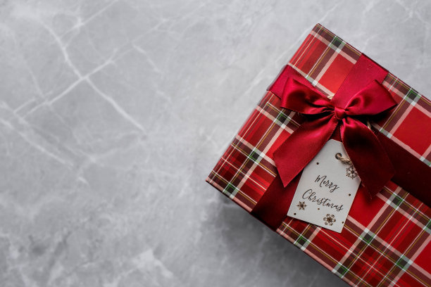 一个装在笼子里的红色礼品盒和一个灰色大理石背景上写着“圣诞快乐”的标签。2023年圣诞节。为家人和亲戚购买和准备礼物。图片下载