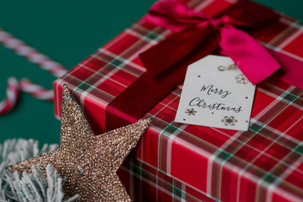 一个装在笼子里的红色礼品盒，一个写着“圣诞快乐”的标签，绿色背景上有冷杉树枝。2023年的圣诞节。传统的颜色。为家人和亲戚购买和准备礼物。图片下载