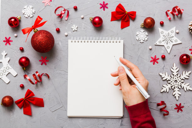 女人写圣诞做清单在笔记本上彩色背景与圣诞装饰图片下载