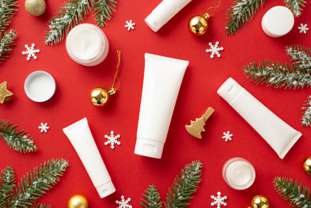 冬季护肤理念。俯视图照片白色管奶油罐杉木树枝在白霜金色的小饰物装饰夹和雪花孤立的红色背景与复制空间图片下载