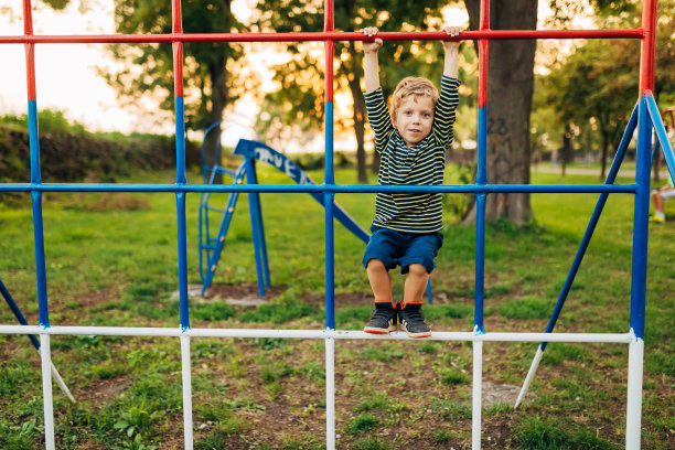 这个可爱的小男孩在公园里爬单杠玩得很开心图片下载