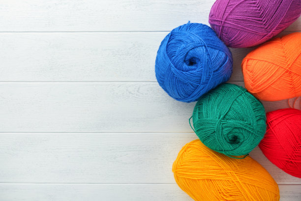 许多彩色球线针织织物上的白色木制背景。鲜艳的花纱，编织和钩针。针线活或针织概念。图片下载
